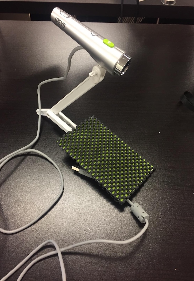 Image of a mobile phone holder with a mounted camera that points down so the viewers can see what the user of the phone is doing on the screen.